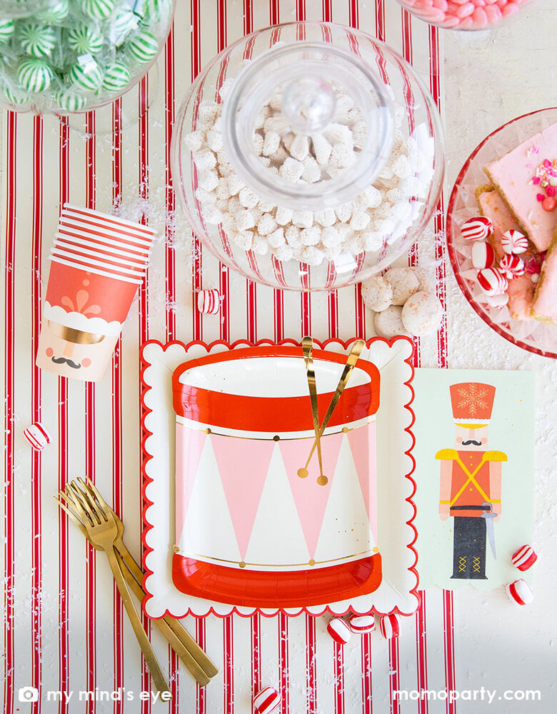 Holiday Christmas Table set up with My Mind's Eye Nutcracker Drum Shaped Plates layered with Believe White & Red Scalloped Large Plates, with Nutcracker Napkins and Nutcracker Soldier Cups, candy canes, a jar with sweets, cookies, and golden folks over the Believe Christmas Red Striped Table Runner. These Morden and high quality party supplies with cute design in pink and red tone are perfect for holiday family celebration with kids. Shop Holiday partyware, party supplies at momoparty.com