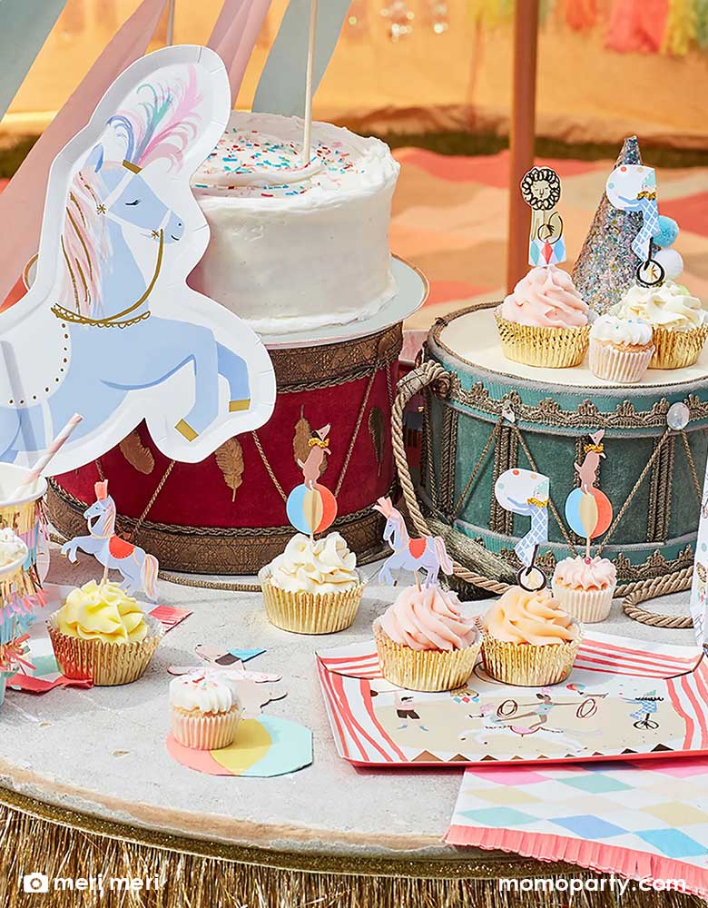 A circus themed party table with Meri Meri's circus parade tableware collection including a 9.25" big top tent shaped dinner plate, circus themed cupcake toppers, pony-shaped plates and some circus drums as the props, all makes a great inspiration for a kid's circus or carnival themed birthday party look.