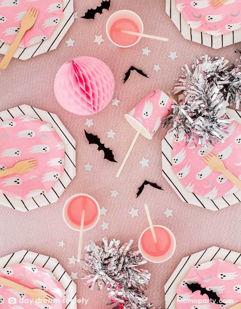 A pink party table with Daydream Society_Halloween Spooked Party Supplies with adorable ghost design on a neon pink background, along with sliver star shaped confetti, bat decorations and silver streamer, a perfect table scape inspiration for a kid's friendly not-so-spooky Halloween celebration