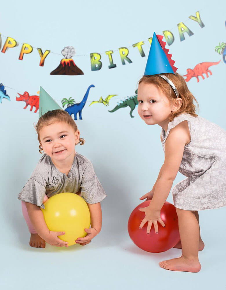 Kids in a dinosaur themed birthday party wearing Merrilulu's Dinosaur Party Hats with spikes in green and blue
