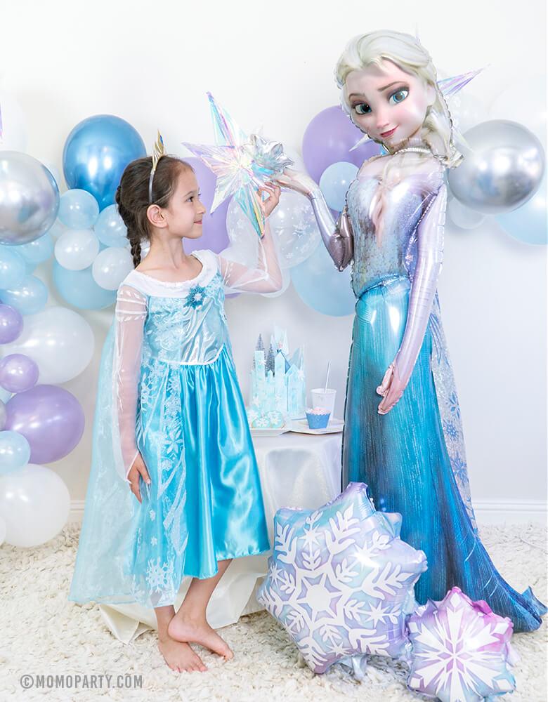 Girl wearing Elsa costume stand next to 57 inch Anagram_Disney Frozen Elsa Airwalker Foil Balloon and Holographic Snowflake Cluster Foil Balloon in a Frozen birthday party