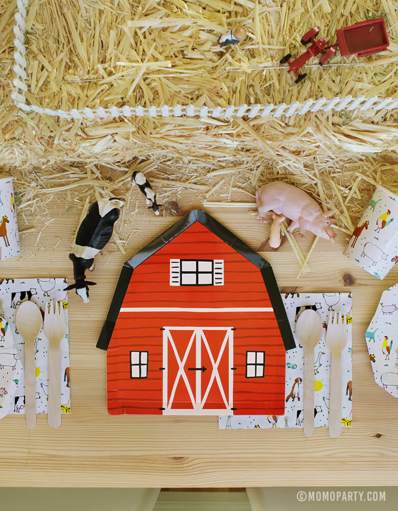 Kids Farm Barnyard Party table set up with Red Barn house plate in the middle, on the Farm-Animals Small Plates, wooden utensils on top of Farm-Animals Napkins, Paper Cups, animal toys on the Straw Bale as center piece