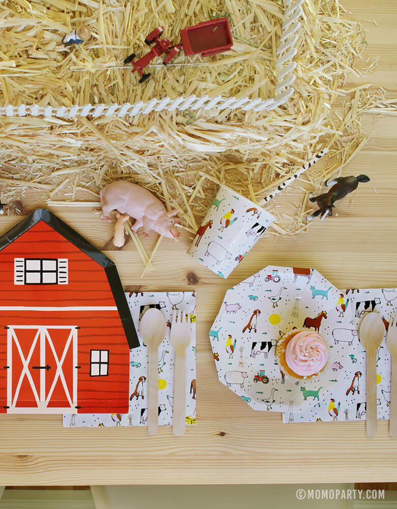Kids Farm Barnyard Party table set up with cupcake on the Farm-Animals Small Plates, wooden utensils on top of Farm-Animals Napkins, Paper Cups, Red Barn house plate, animal toys on the Straw Bale as center piece