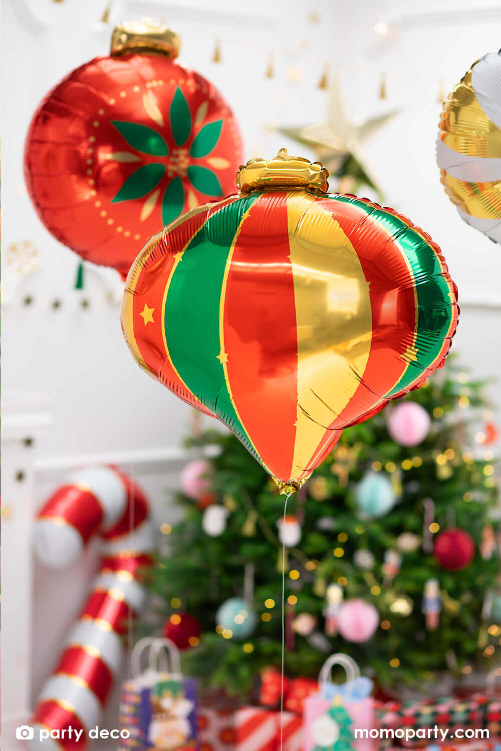 Holiday home decoration with Festive Christmas Ornament Foil Balloon in a classic teardrop shape ornament with green, red and gold color, and Red Christmas Ornament Foil Balloon in the middle of the room, there are christmas tree decorated with lots of ornaments, lights, gifts under it for a holiday celebration.