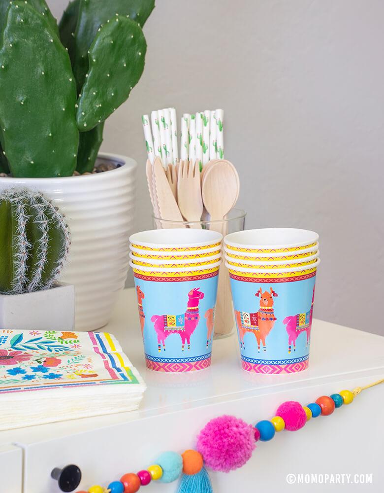 A conner of a party dessert table with Talking Tables Boho Fiesta Llama Cups, Hyper Tropical Wooden Cutlery Set, Cactus printed paper straws, Boho Fiesta Floral Napkins and Boho Fiesta Pom Pom Garland for A Boho Fiesta Themed Party, or Modern Cinco De Mayo Party