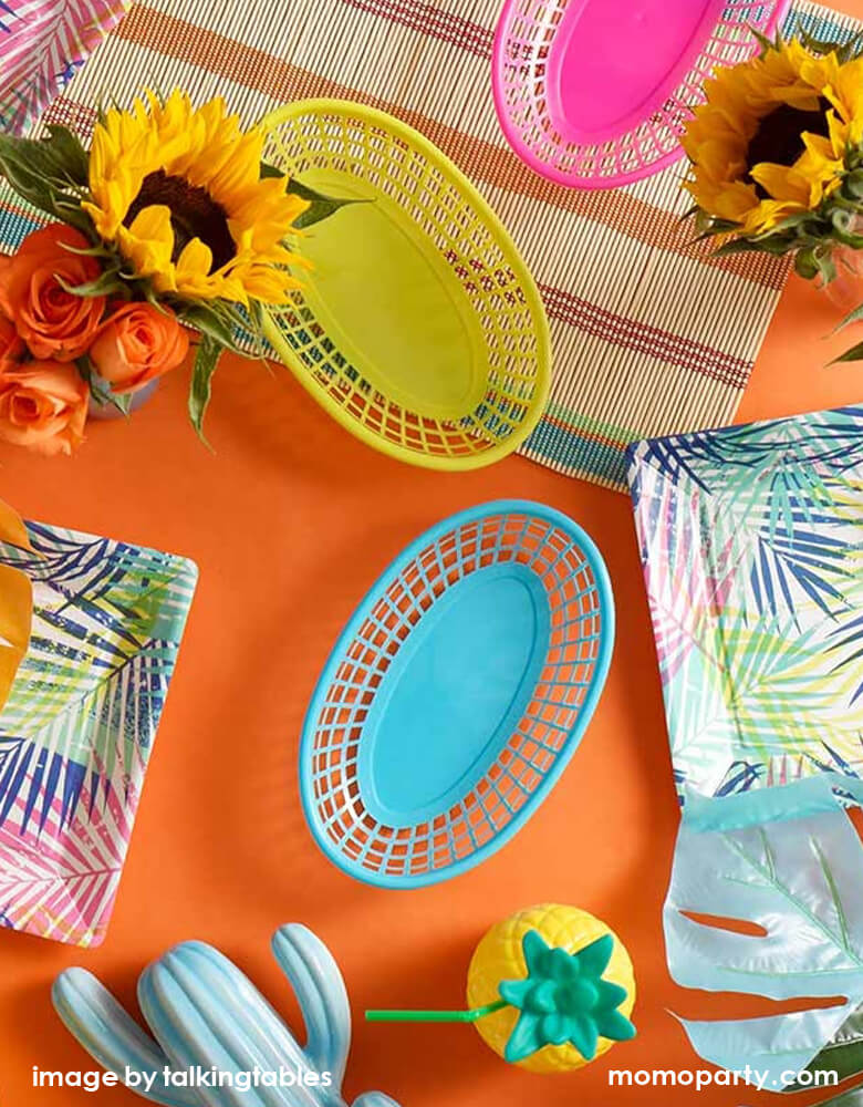 Fiesta themed party table decorated colorful Cuban-inspired food baskets in bright yellow, pink and blue color, pineapple sipper, sunflowers, cactus ceramic, table cloth and tablewares