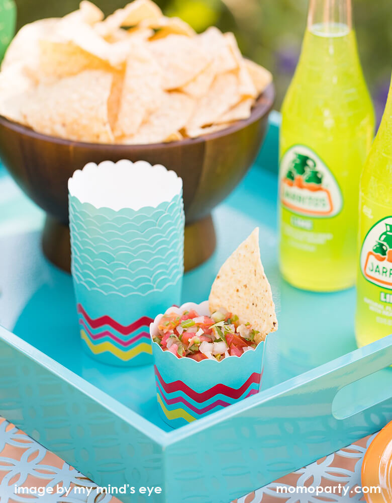 Fiesta party table with a bowl of chips, Jarritos Soda, chips and salsa in the My mind's eye Fiesta Food Cups in a mint blue tray for a fun summer party