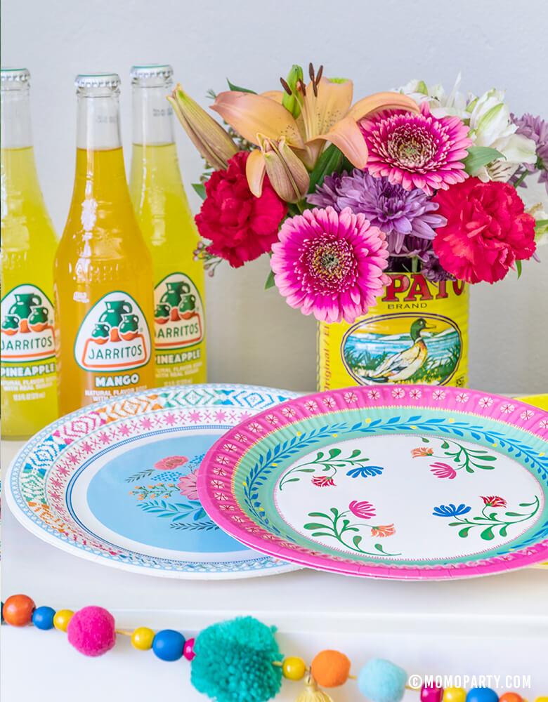 Talking Tables 9" Boho Fiesta Floral Plates, with Boho Fiesta Pom Pom Garland, Flowers inside of salsa cans, Jarritos Mexican soda for A Boho Fiesta Themed Party, or Modern Cinco De Mayo Party