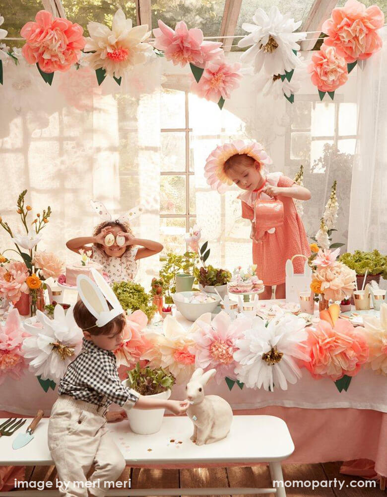 Kids dressed up with Blossom Crowns, Bunny Ears, playing and decorated eggs in a Sunroom decorated Meri Meri Flower Garden Giant Garland, lot of fresh flowers, sweets for a Flore Easter Spring party