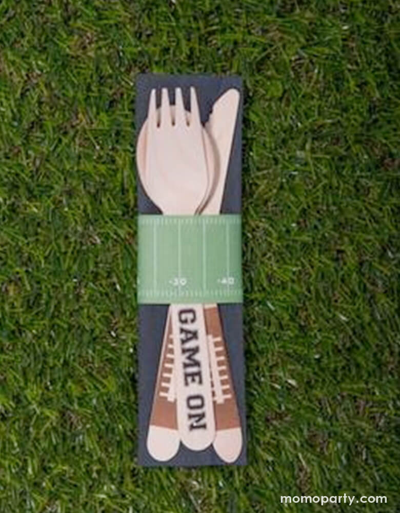 Game day party set up with Football Game On Wooden Cutlery set over a grass tablecloth. This cutlery kit is perfect for your football themed celebration! Each kit comes with 8 birch utensil sets (spoon, fork, knife) with football and game on printing, 8 paper football field print napkin rings, and 8 black paper napkins.