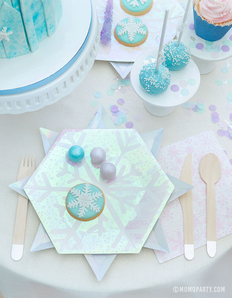 Frozen Inspired party supplies of Snowflake-designed plates, napkins, silver utensils on a whimsical table of party treats for a kids birthday party