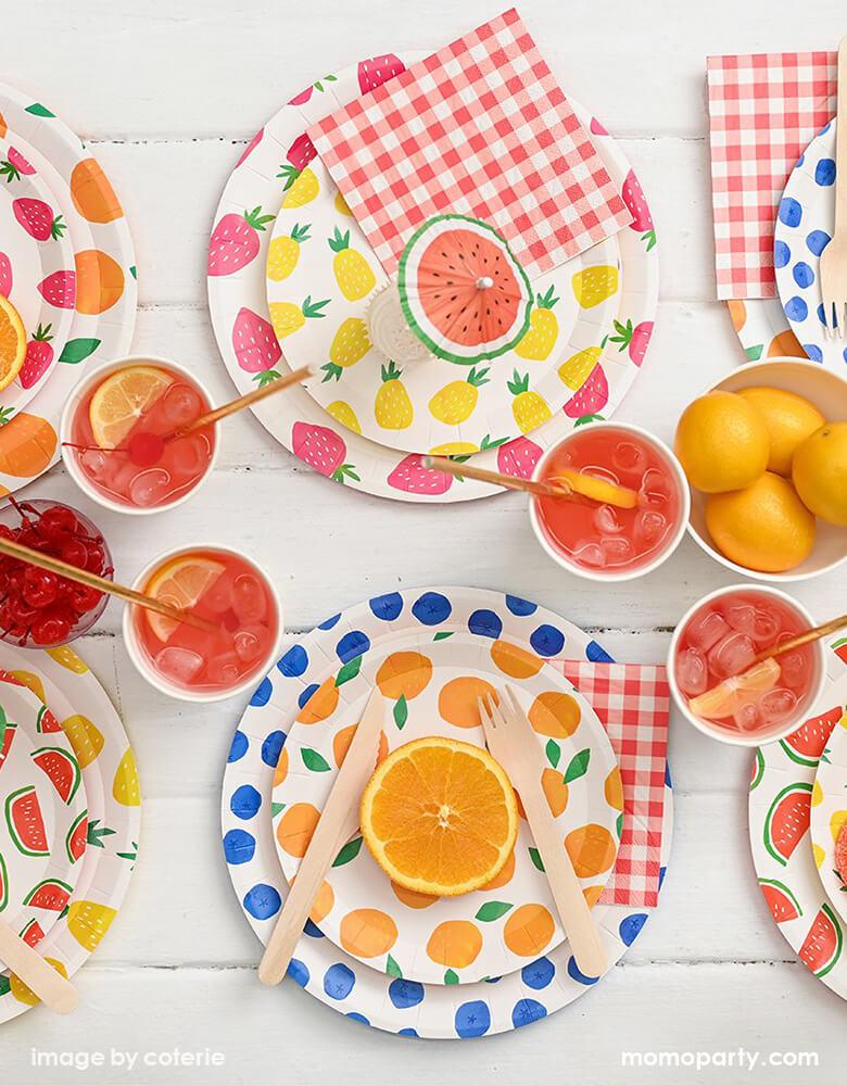 Summer Fruity Party table filled with layered Fruit Punch Large and Small Plates, red-and-white gingham Summer Picnic Small Napkins, wooden cutlery, soda with sliced lemon in cups, orange, lemon, watermelons on the plate with watermelon umbrella topper. These modern designed Bright and fun partyware are perfect for any summer parties