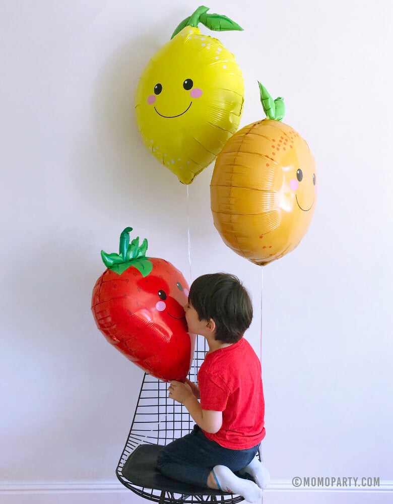 boy sitting under lemon and orange foil balloons and kissing Strawberry Foil Mylar Balloon