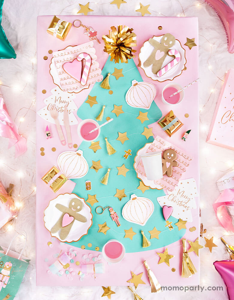 An adorable pastel Christmas themed party table filled with Party Deco's pink Christmas tableware including gingerbread man napkins, Christmas ornament napkins, pastel colored confetti and gold star banners  on a mint Christmas tree shaped table runner 