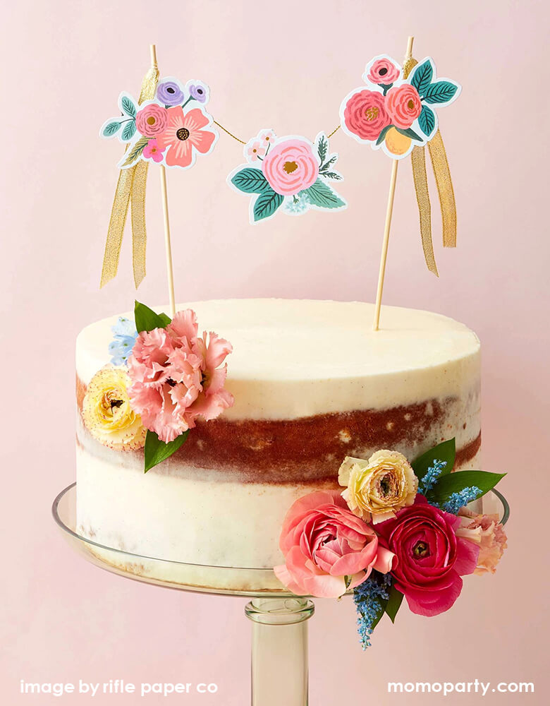 A modern naked cake decorated with Rifle Paper Co - Garden Party Cake Topper and fresh flowers.. This garden party cake topper featuring Blooming floral clusters are strung between two posts, with gold ribbon ties and gold foil accents, it adds a colorful finishing touch to any cake.