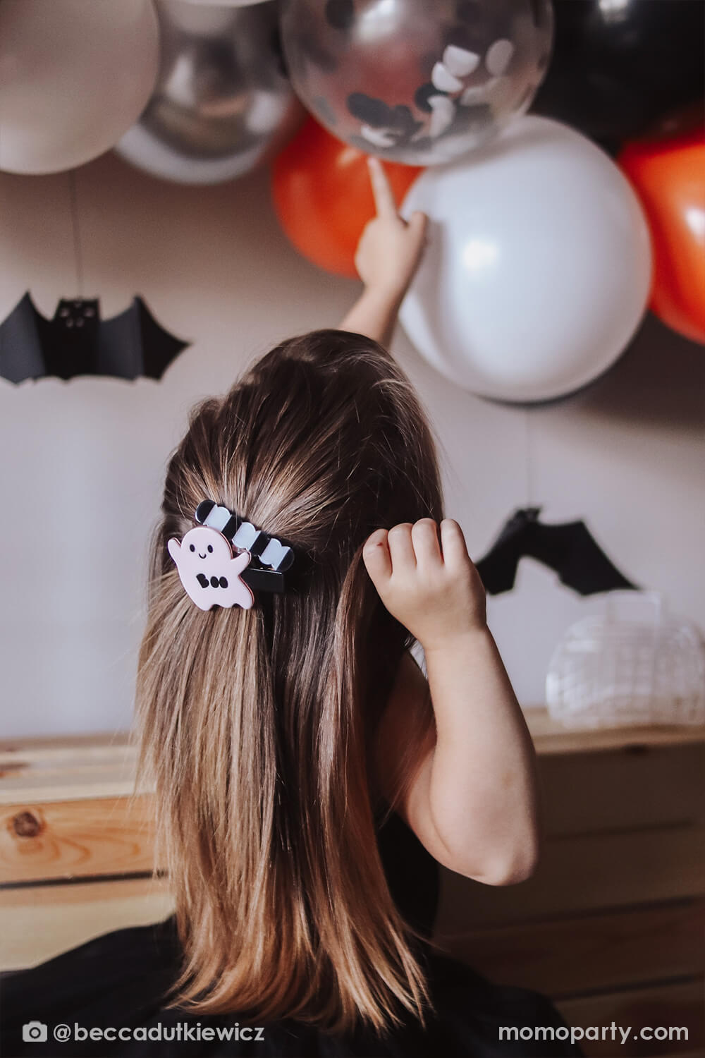 Girl wearing black tutu dress and her ponytail tied with Ghost Light Pink + Wave Black Stripe Alligator Hair Clips, pointing to Meri Meri Halloween Balloon Garland, mixed with black, silver, orange, white and confetti balloons and hanging bat decoration. These Beautiful and affordable halloween Accessory and party decorations, party supplies are spooktacular fun for your Halloween bash. Find theme in party boutique online store at momoparty.com