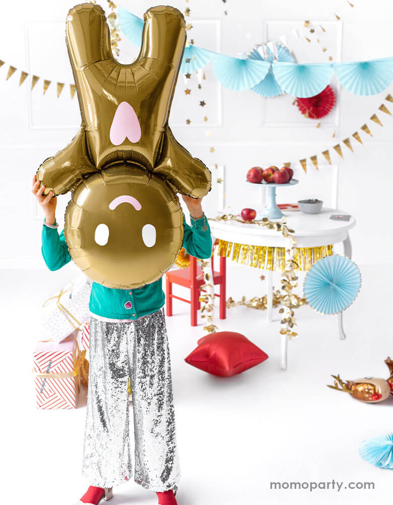 A little girl in festive Christmas themed outfits holding Party deco's 34" Gingerbread Man Foil Balloon upside down with Christmas decorations in the background 