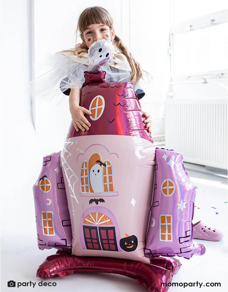 Girl holding Party Deco 35x46 inches haunted house shaped standing foil balloon with cute ghost illustrations in pink and iridescent details, a perfect decoration for a girly pink Halloween party