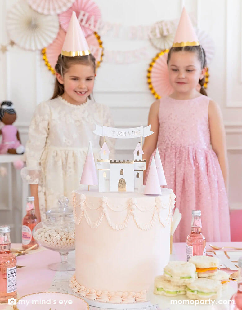 A party table with princess themed birthday cake in a room decorated with princess themed decorations in beautiful pink and gold