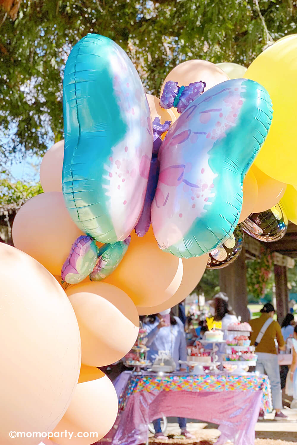 Momo Party's 29" Flutters Butterfly Foil Mylar Balloon on a pastel rainbow balloon arch in a girl's fairy themed birthday party.