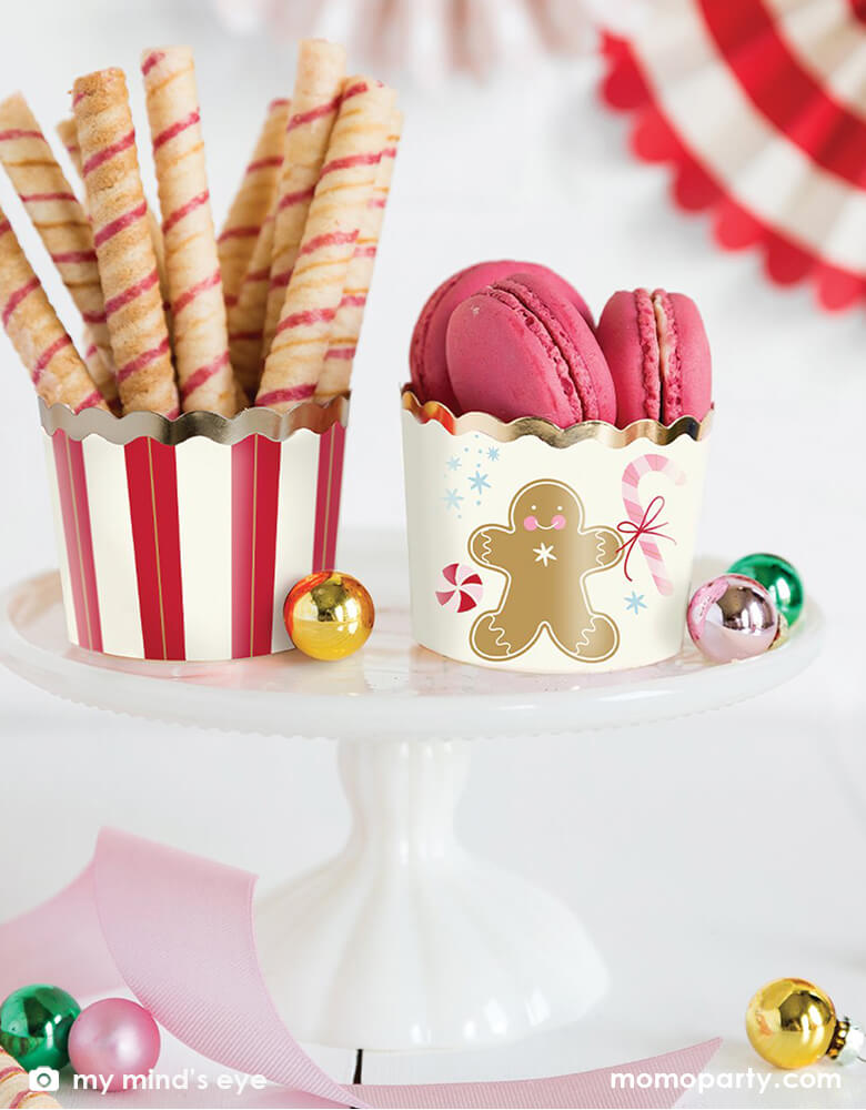 Holiday table close up with sweets inside the My Minds Eye - Gold Foil Gingerbread Man Food Cups on a white cake stand with colorful bells around. Featuring in 2 designs with gingerbread man with candy canes design, and red white stripes with gold foil edge. These adorable gingerbread man food cups are perfect for baking cupcakes right in the oven. Add candy and wrap in cellophane for a holiday neighbor gift, cut up veggies and add dip for the perfect hors d'oeuvres at a party or fill with fun snacks!