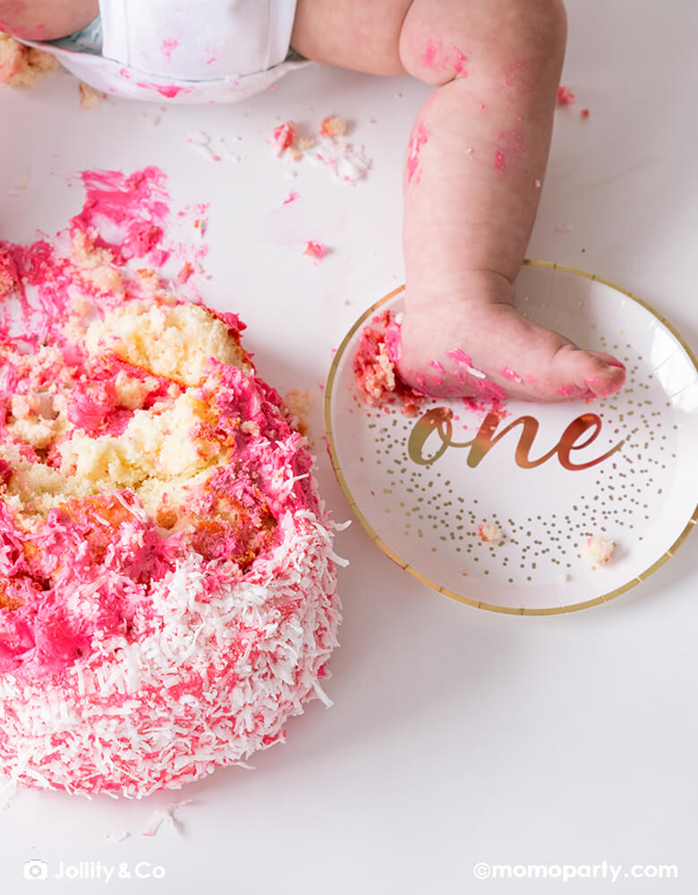 First birthday pink smash cake with Jollity 7-inch onederland gold round dessert plate with gold script "one" on it and gold foil confetti illustration around it, it's gender neutral and perfect for baby's first birthday party celebration!
