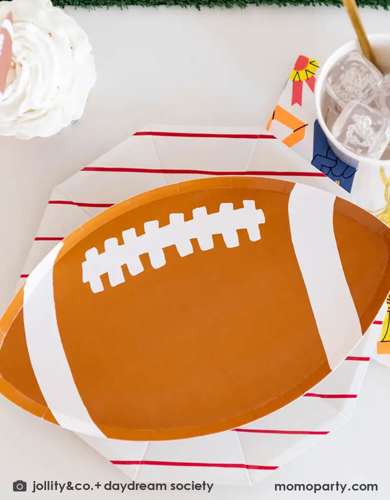 A close up of a sports themed party table featuring Momo Party's 7.5" good sport football shaped plates by Daydream Society. Come in a set of 8 plates, you can use these plates for team parties, birthday parties, and the Super Bowl! Go team!