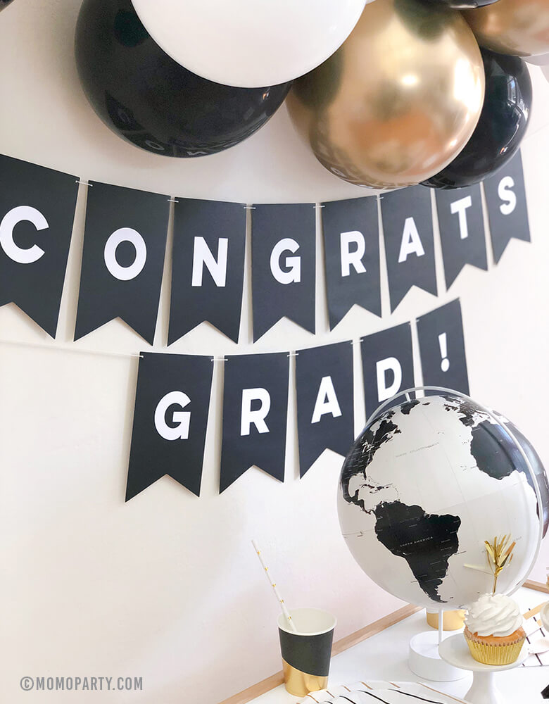 2020 Graduation at home celebration with  Black banner with "Congrats Grad!" sign and black and white Globe, Balloon garland with gold, black, white as wall decoration