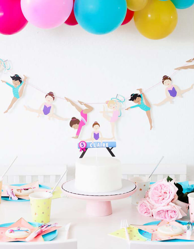 Girl's Gymnastics Themed Party Set with Merrilulu Gymnastics Garland, Ballon garland, Custom Gymnastic Cake topper over a white cake, MeriMeri Star Plates, cups, Oh happy day blue plates,  table and decorations styled by Twinkle Twinkle Little Party