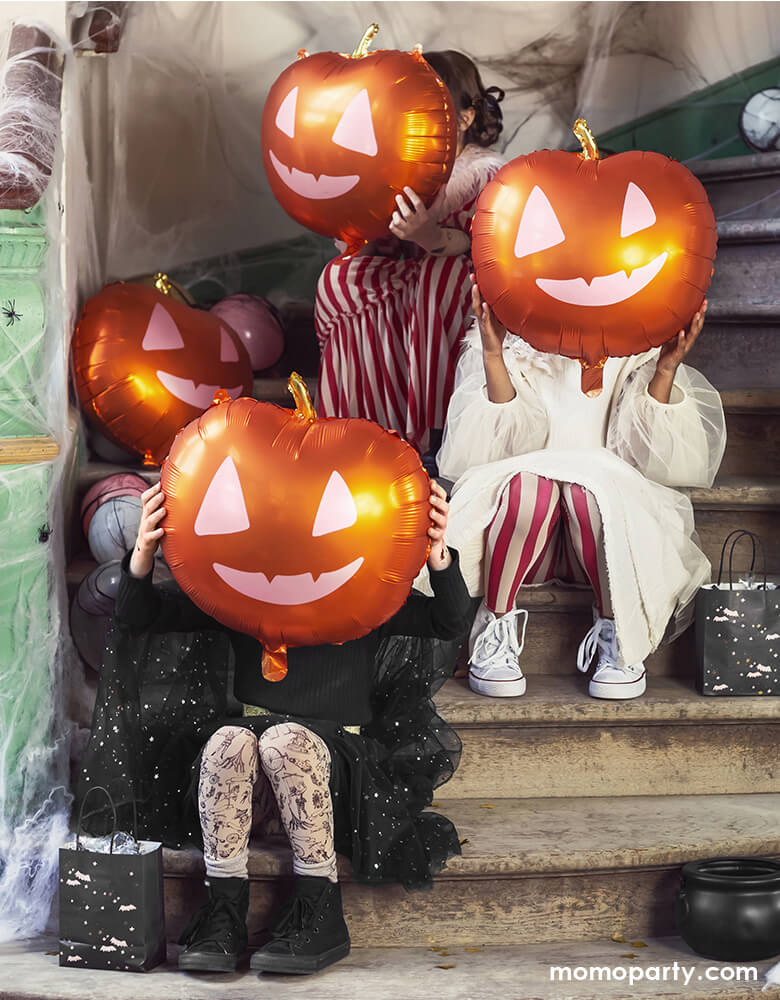 Girls sitting on the stairs with holding Party Deco 16 inches Halloween Pumpkin Foil Mylar Balloons to cover their faces, these pumpkin foil balloons featuring a pumpkin shape in orange and gold foil color with Jack O'lantern happy face in pink, Bring this cute Jack O'lantern balloon to your Not-So-Scary Halloween Party!!