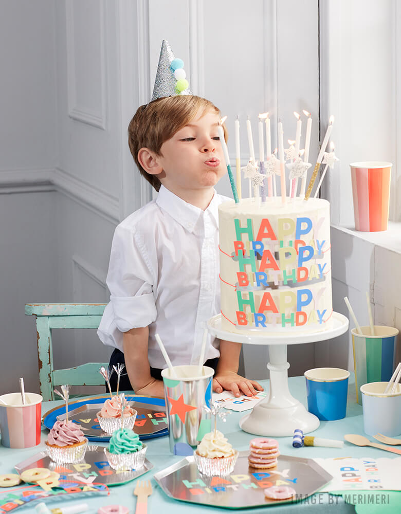 boy blowing candles on his birthday with  Meri Meri Silver Happy Birthday Palette Side Plate with multi-color texts on it on the table