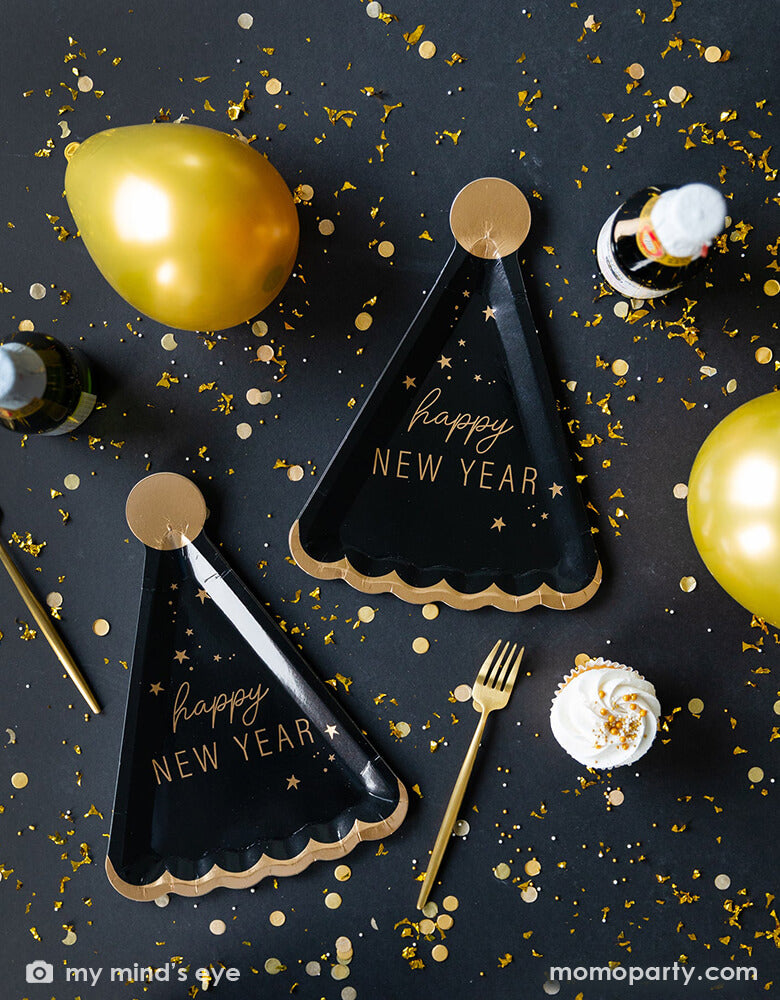 New Year's Eve countdown party table filled with Momo Party's 10 x 7 inches Happy New Year Hat Shaped Plates by My Mindy's Eye, featuring black and gold foil accents, with the message of "Happy New Year", gold confetti, gold forks and gold latex balloon and champagne. 