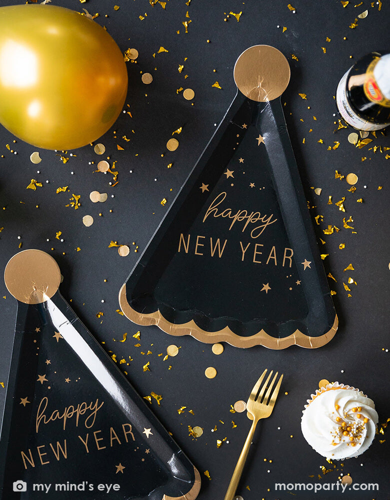 A close up New Year's Eve countdown party table filled with Momo Party's 10 x 7 inches Happy New Year Hat Shaped Plates by My Mindy's Eye, featuring black and gold foil accents, with the message of "Happy New Year", gold confetti, gold forks and gold latex balloon and champagne.