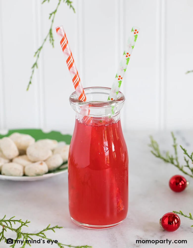 A holiday table with a cranberry juice bottle with Momo Party's Holly Reusable Straws by My Mind's Eye featuring festive Holly designs and Candy cane red stripes on the straws, perfect for this holiday season!
