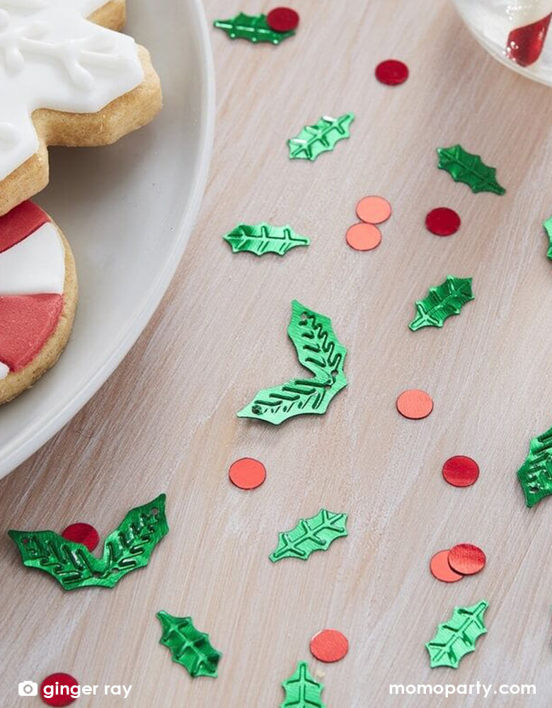 Holiday table close up with Ginger Ray - holly shaped christmas table confetti on the table next to a plate with christmas cookies. Sprinkle some festive fun on your Christmas table this year with this fun Christmas holly shaped table confetti. The foiled cut out design of green Christmas holly shape and red circle are perfect for adding that glitzy feel to your home.