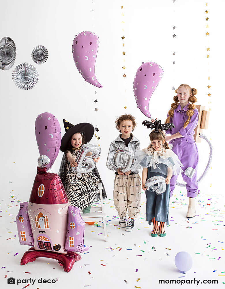A bunch of kids dressed up for Halloween in different fun costumes holding Party Deco's purple ghost shaped foil balloons with a 35x46 haunted house shaped standing foil balloon with cute ghost illustrations in pink and iridescent colors, a perfect idea for kid-friendly Halloween celebration