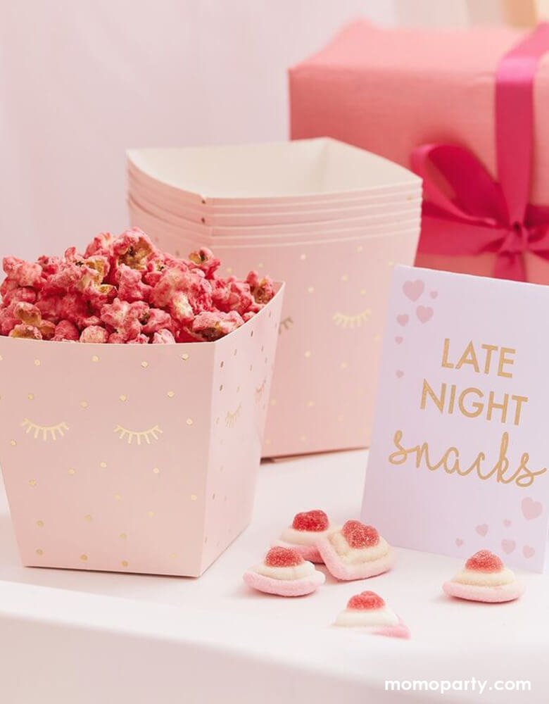 Momo Party's LATE NIGHT SNACK BAR MIDNIGHT FEAST KIT by Ginger Ray. There are pink popcorn In the treat boxes with sweet eyelid and dots in a gold foil print, and a 1 tent card with "late night snacks" text and heart print on the side, heart shaped candies on the table. These modern and cute design party supplies from Meri Meri of cat and Dog collection, are perfect decoration for a kitten or cat themed birthday party for kids or adults.