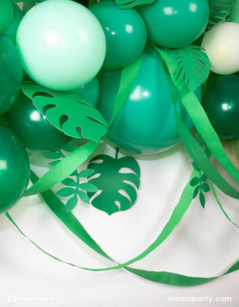 A closeup of Meri Meri leafy balloon arch including 44 balloons, including 44 balloons in the different shades of green, gold and ivory, paper leaves and crepe paper streamers, it is the perfect backdrop for a safari, jungle, or dinosaur party.