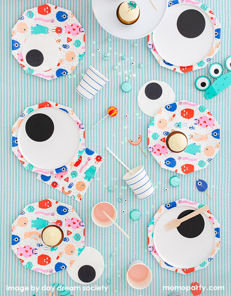 Little Monsters themed party table top view with Daydream Society Little Monsters Eyeball plates layered with Little Monsters Large Plates, and Little Monsters Large Napkins, Little Monsters Eyeball Small Napkins and blue stripe cups, Little Monsters Party Headband Set, all on top of the mint stripe tablecloth for a modern cute little monster themed birthday party, halloween party