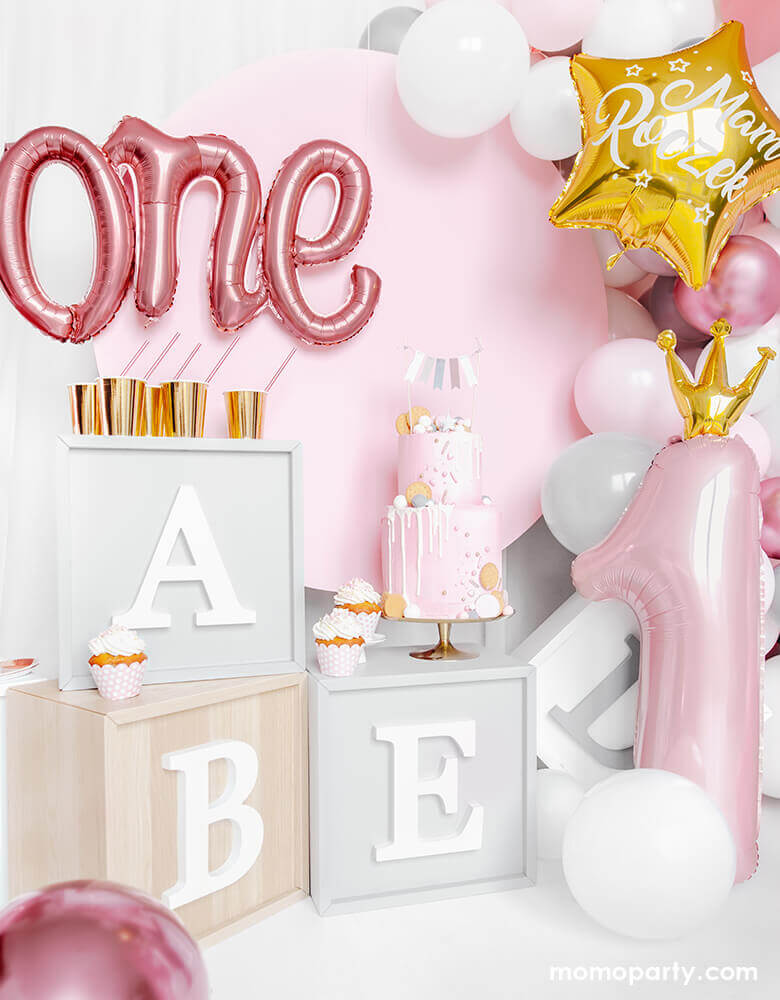 Adorable first birthday party decorated with Alphabet letter blocks, Rose Gold One Script Foil Balloon, a 2 tire pastel pink cake with flag topper, cupcakes, lots of pink and white latex balloons, and  a 35 inch Little Crown Number 1 Pastel Pink Foil Balloon by Party Deco on the side. This adorable party set up is prefect for your baby first birthday party, baby 1st year's photoshoot, 1st year celebrations! It's a great way mark your little princess' big milestone! 