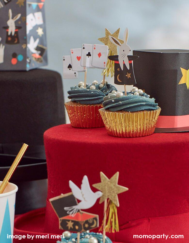 magic themed party staged with cupcakes decorated Meri Meri Magic Cupcake Kit with gold glittering stars, cards, rabbits popping out of a hat and doves toppers, and magic hat, party bags around