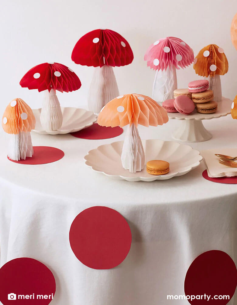 Meri Meri's Honeycomb Mushroom Decorations on a party table with scallop shaped party plates and pink shade macarons, the table cloth is decorated with red and white polka dots  a perfect look for kid's fairy or woodland themed birthday celebration 