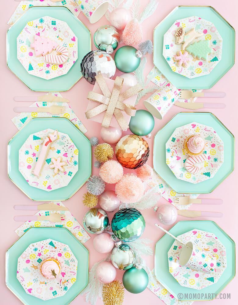 Modern Pastel Christmas Holiday Party Table Set up for 6 people with Meri Meri Mint Large Dinner Plates, Daydream Society Merry and Bright Holiday Christmas Party Plates, Napkins and Cups, Pink wooden utensils and Pastel colored Sisal Trees, and Ornaments as centerpiece