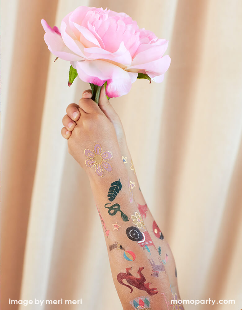 a kid holding a flower with  full of fun bright colors with shimmering silver foil detail temporary Tattoos on her arms