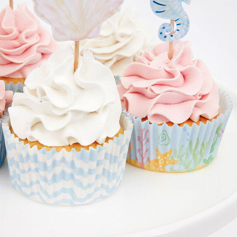 close up details of Pink and white cupcakes decorated with Meri Meri mermaid cupcake kit. With beautiful mermaids, a seahorse and seaweed toppers and pastel blue color cupcake cases.