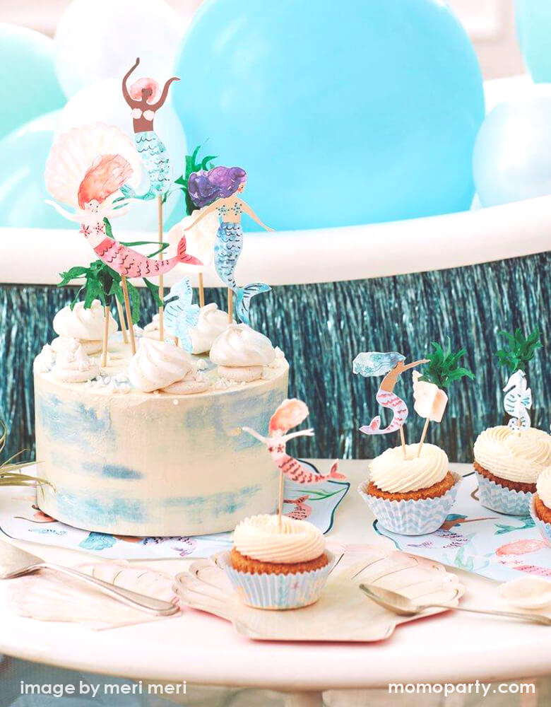 Detail look of a Modern Mermaid Party, There are Meri Meri Mermaid Swimming Plates, Watercolor Clam Shell Plates holding up cupcakes with Mermaid Cupcake toppers, Watercolor Seashell Napkins next to them, A naked cake decorated with Mermaid Cake Toppers. with Mixed blue,teal mint colored latex balloons and blue fringe garland behind it. What a fun dreamy mermaid party for eight kids birthday, or who love mermaid, or a under-the-sea party celebration