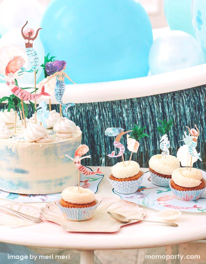 Detail look of a Modern Mermaid Party, There are Meri Meri Mermaid Swimming Plates, Watercolor Clam Shell Plates holding up cupcakes with Mermaid Cupcake toppers, Watercolor Seashell Napkins next to them, A naked cake decorated with Mermaid Cake Toppers. with Mixed blue,teal mint colored latex balloons and blue fringe garland behind it. What a fun dreamy mermaid party for eight kids birthday, or who love mermaid, or a under-the-sea party celebration