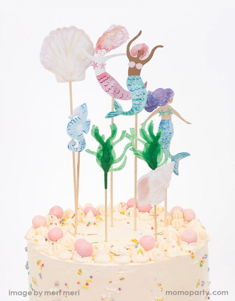 Meri Meri Mermaid Cake Toppers on top of A cream buttercream cake with sprinkles. There are 7 beautifully mermaids, shells and a seahorse in a watercolor illustrated design, the seaweed toppers crafted from green tissue paper. And the rest of the toppers from card, The wooden section is crafted from bamboo. They are perfect for decoratie your birthday cake for an under-the-sea or mermaid party.