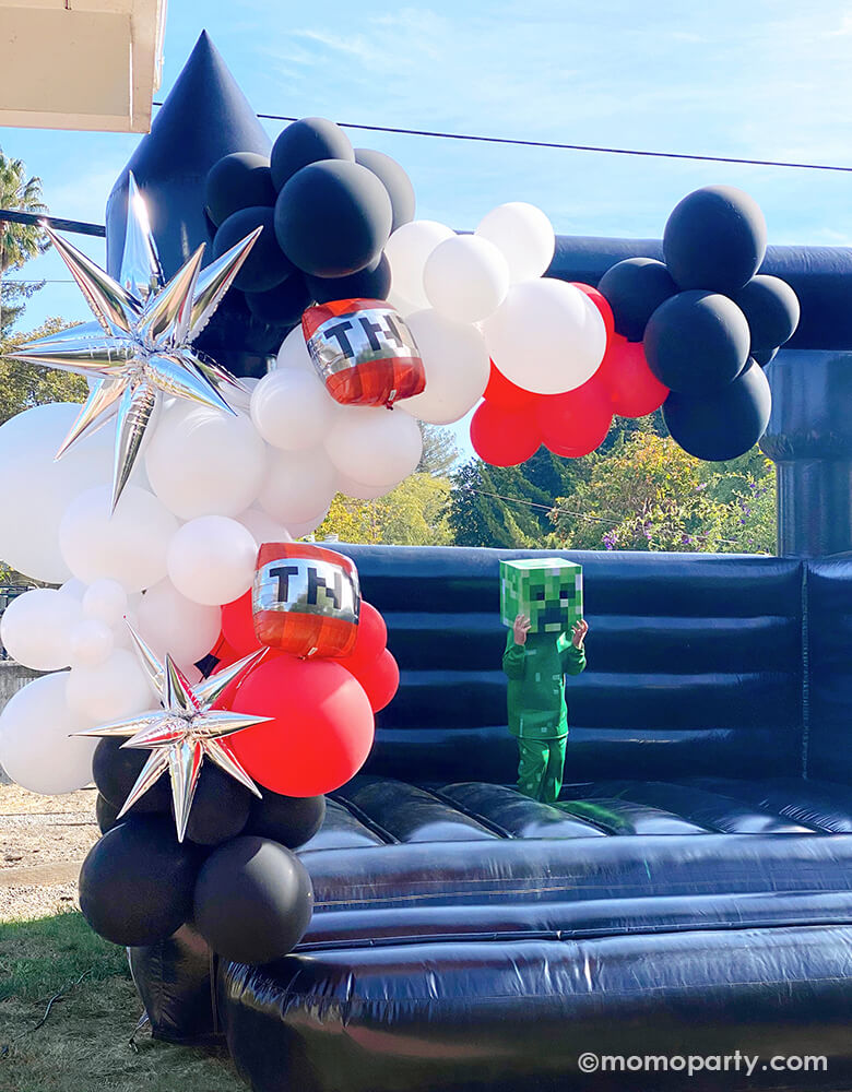 Modern minecraft themed birthday party, a kid wearing creeper costume jumping in a black bounce house, decorated with Black, white, red latex balloons and silver starburst foil balloon and  Minecraft® TNT 8 1/2" Mylar Balloons.