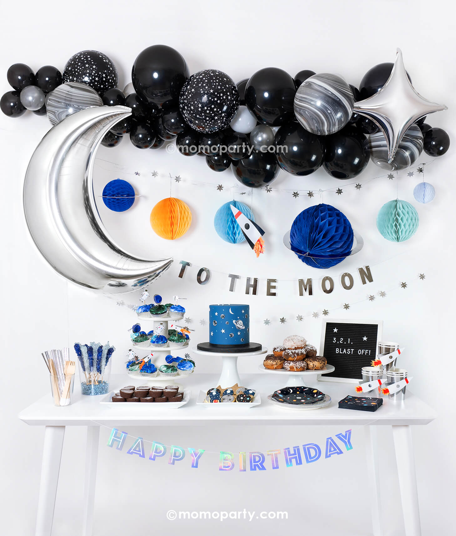 Momo Party's Space Themed Blast Off Party in a Box kit set up with Space themed Balloon garland, Starburst Foil Balloon, Silver Moon Foil Balloon, Honeycomb space garland, Silver Happy birthday banner and tablewares